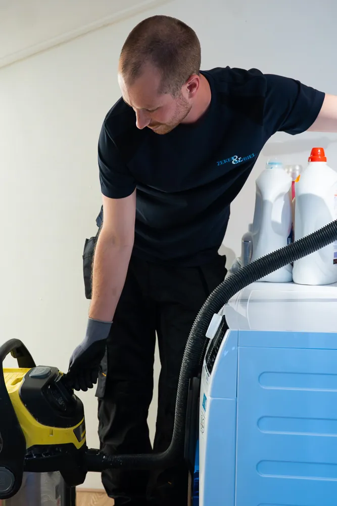 Monteur ontstopt de wasmachine-afvoer met een nat-droogzuiger