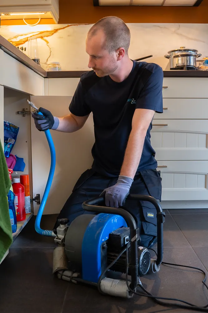 Monteur ontstopt de gootsteenafvoer met een mechanische ontstoppingsveer onder het aanrecht