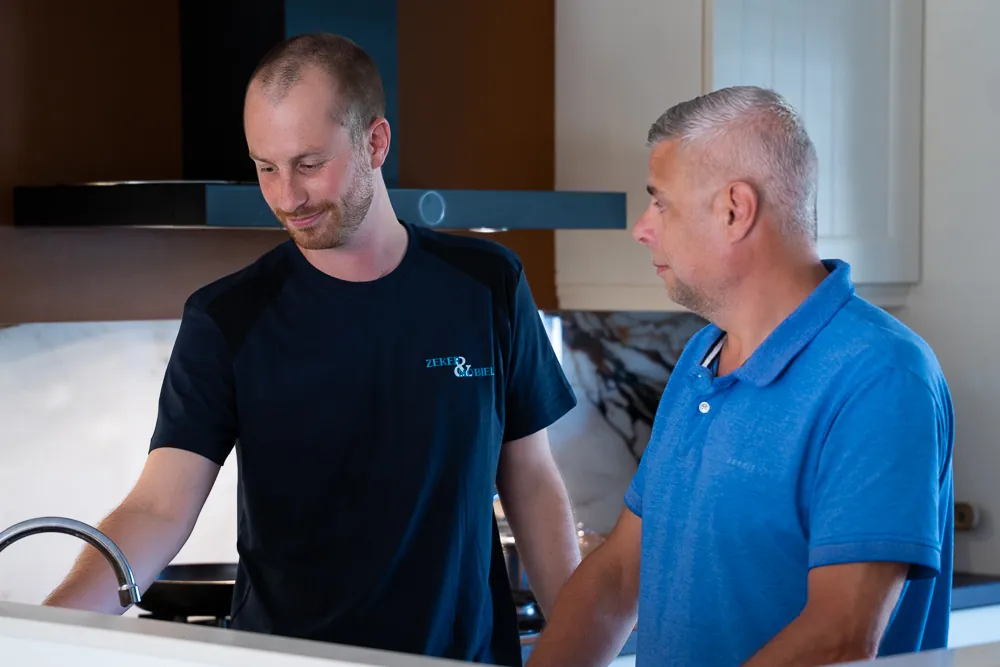 Monteur van Zeker & Mobiel bespreekt een verstopte gootsteen met een klant in de keuken