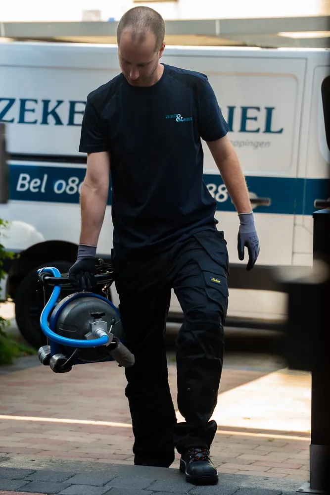 Monteur van Zeker & Mobiel draagt een ontstoppingsmachine van de bus naar een woning in Amstelveen