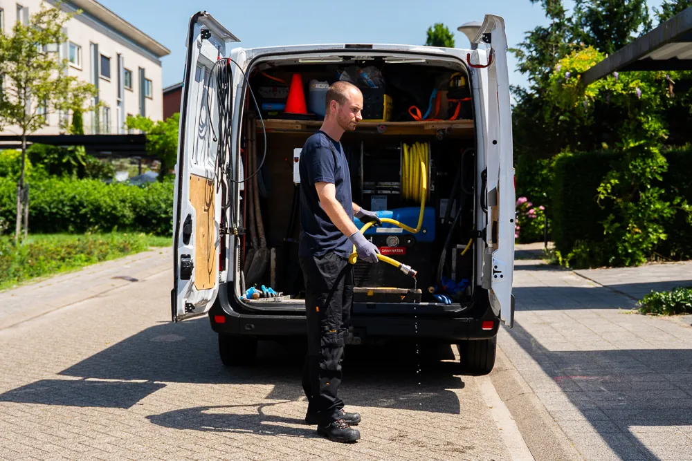 Monteur met hogedrukslang bij de volledig uitgeruste werkbus