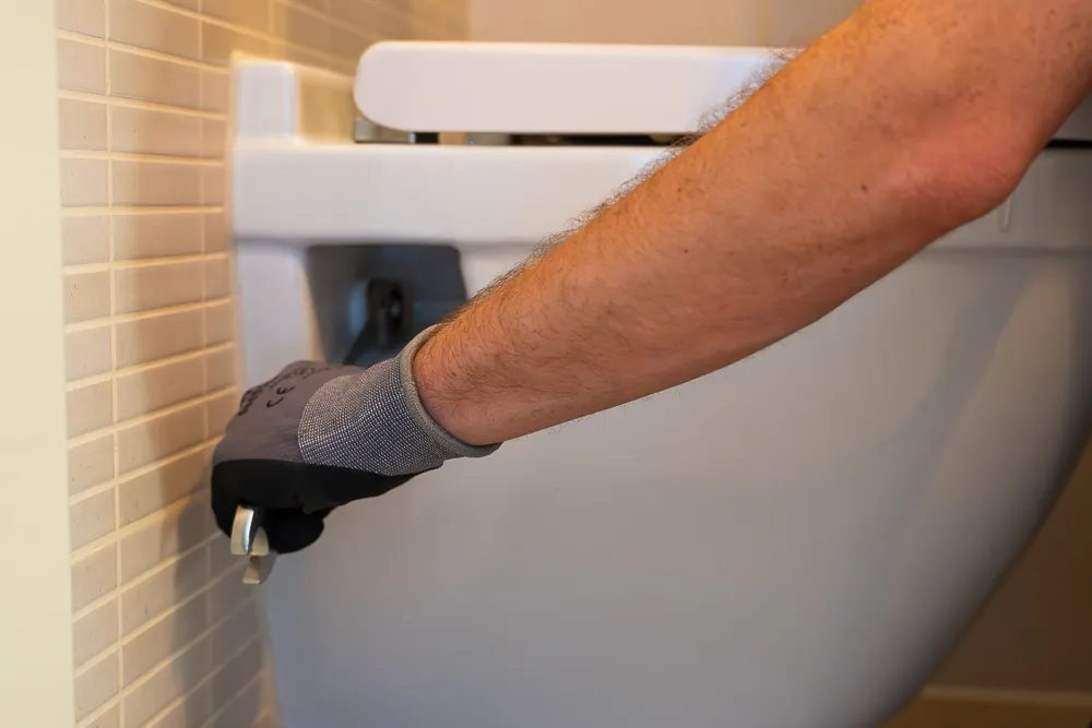 Monteur bij de stopkraan van het hangtoilet om de verstopte wc te ontstoppen